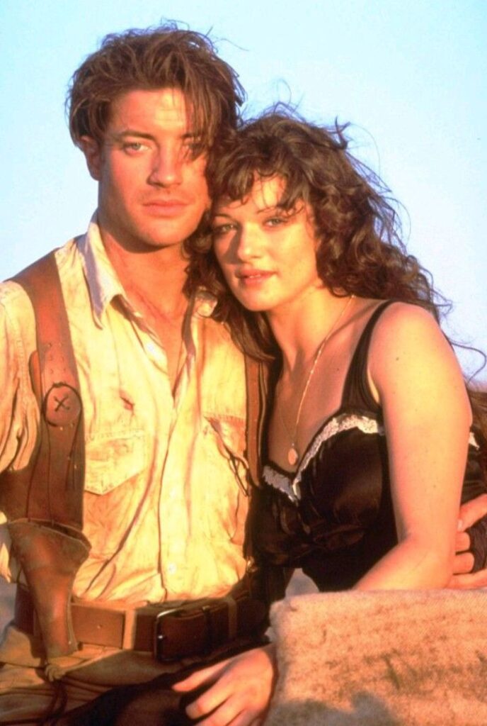 A dramatic desert scene with ruins in the background and a couple standing together. Adventurous and bold with a romantic twist.