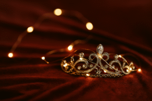 image of a decorative tiara wrapped in fairy lights resting on a cranberry velvet draped surface